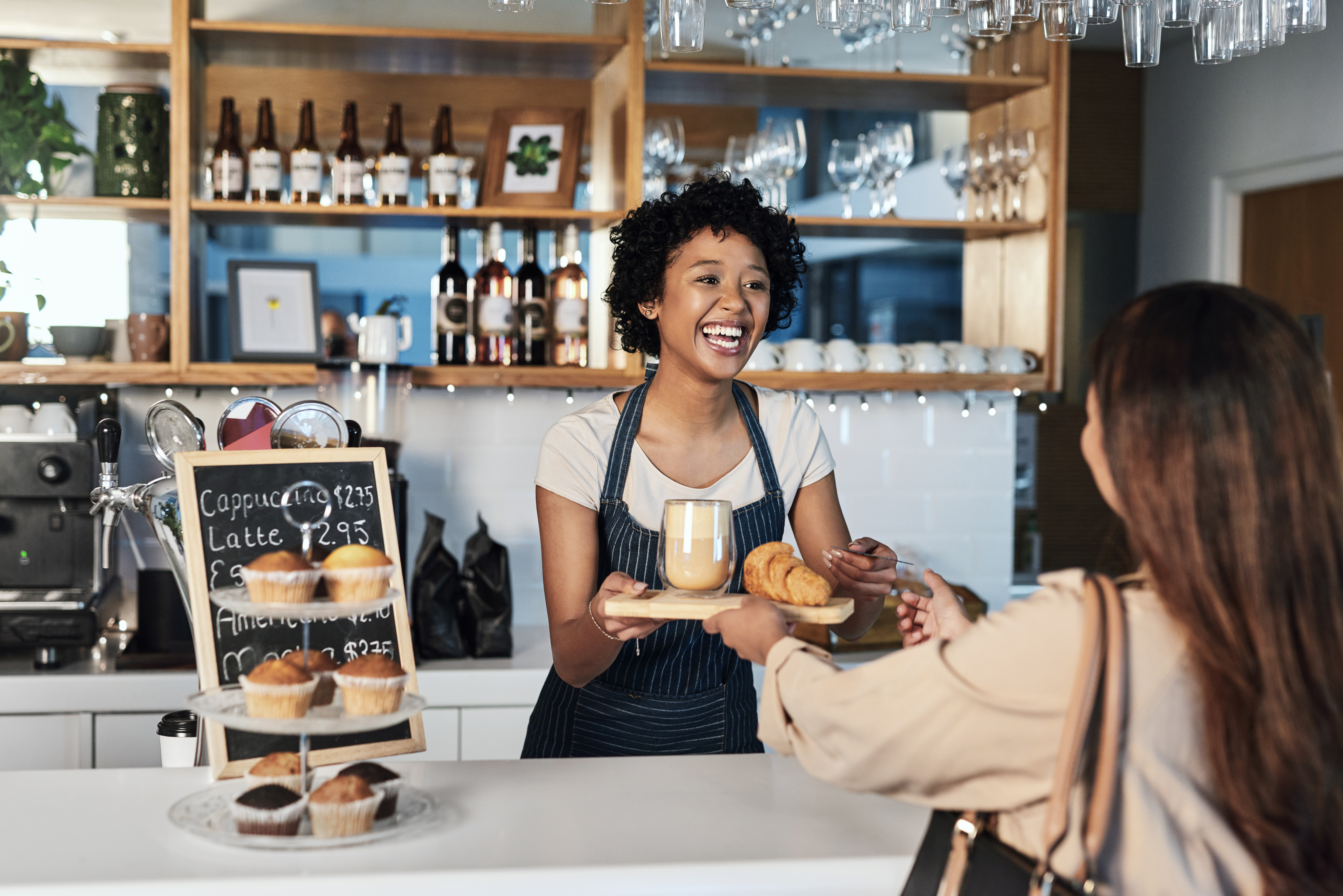 A coffee shop employee handing a customer her order of coffee and a pastry.