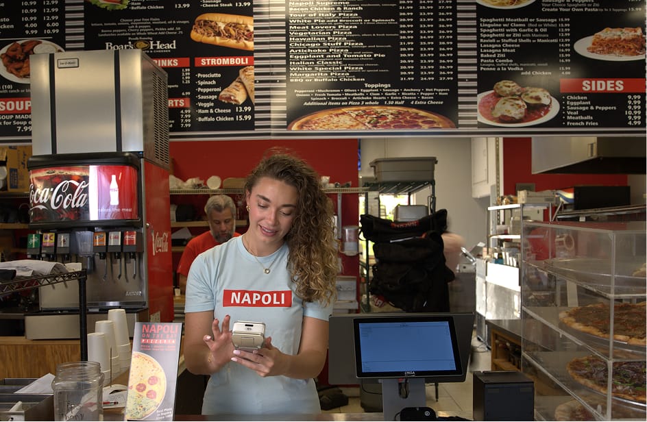 A pizzeria employee using a card reader and customer-facing display screen to take orders.