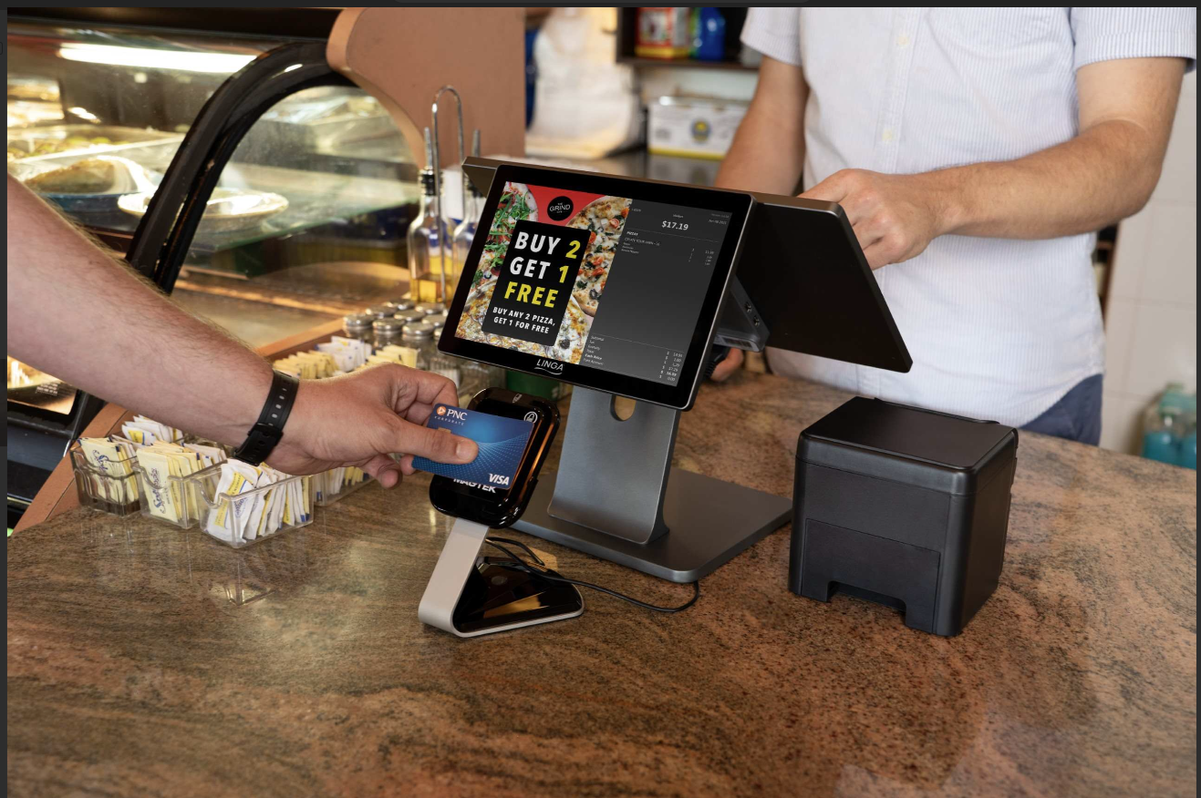 A pizzeria employee using a card reader and customer-facing display screen to take orders.