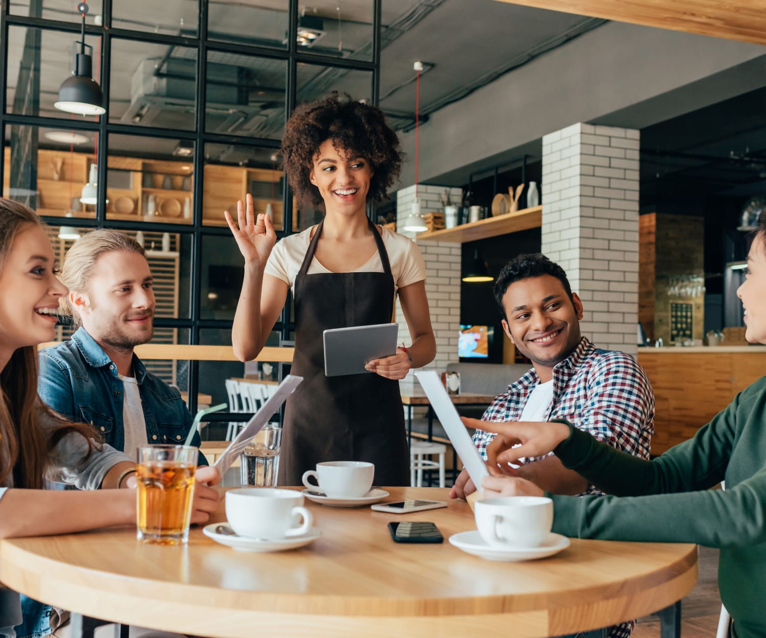 A waitress holding a tablet and taking orders for a group of friends at a cafe.