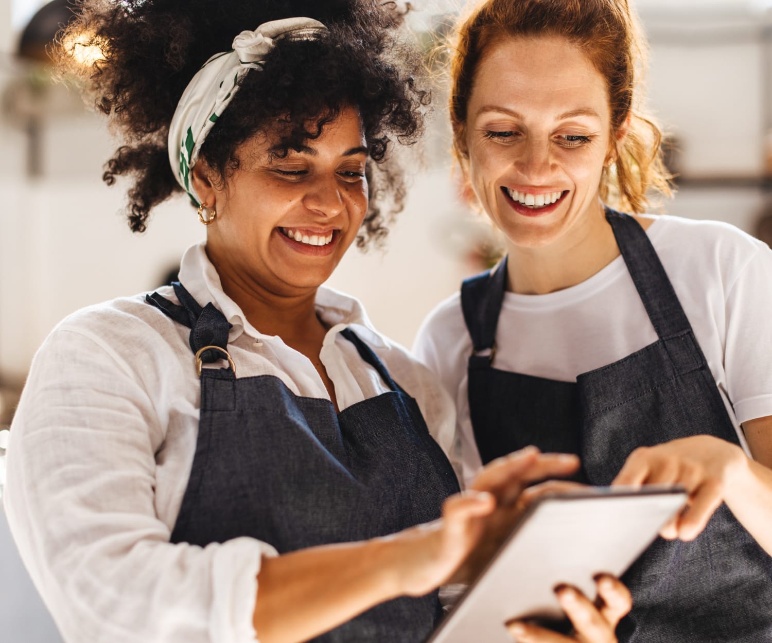 Two smiling restaurant employees using a tablet.